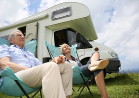 Senior couple relaxing in camping folding chairs, camper in background